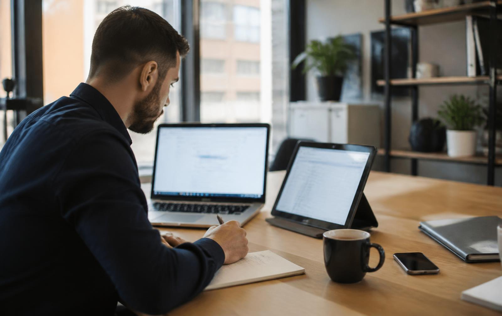 Mitarbeiter arbeitet mit Laptop und Tablet am Büroarbeitsplatz – KI Tools für Unternehmen